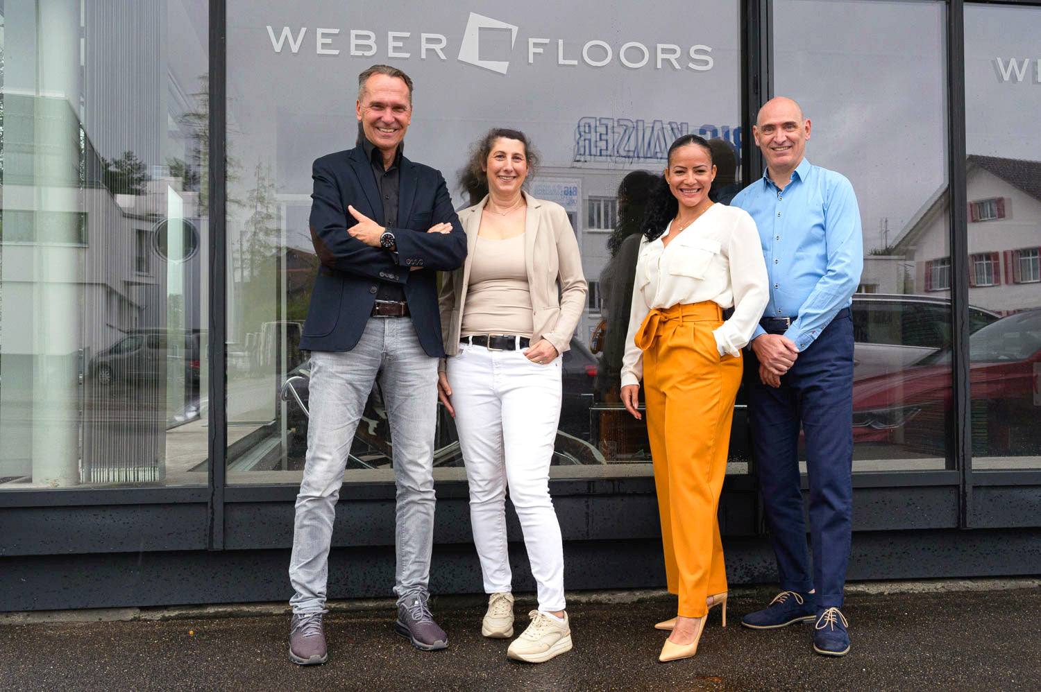 Vier Personen posieren lächelnd vor einer Glasfront mit der Aufschrift "WEBER FLOORS"