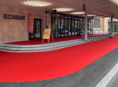 Eingangsbereich außen eines Hotels, der mit zugeschnittenem, roten Teppich für einen Empfang dekoriert ist