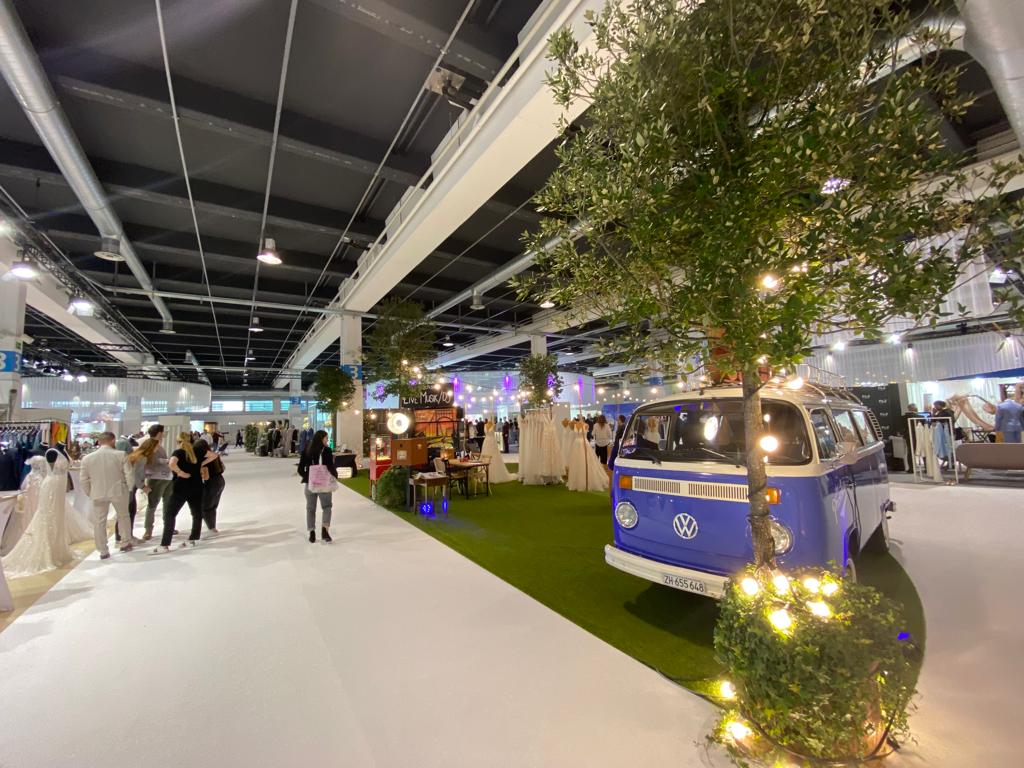 View of the interior of a wedding fair with a VW bus, carpet, artificial turf, trees and fairy lights
